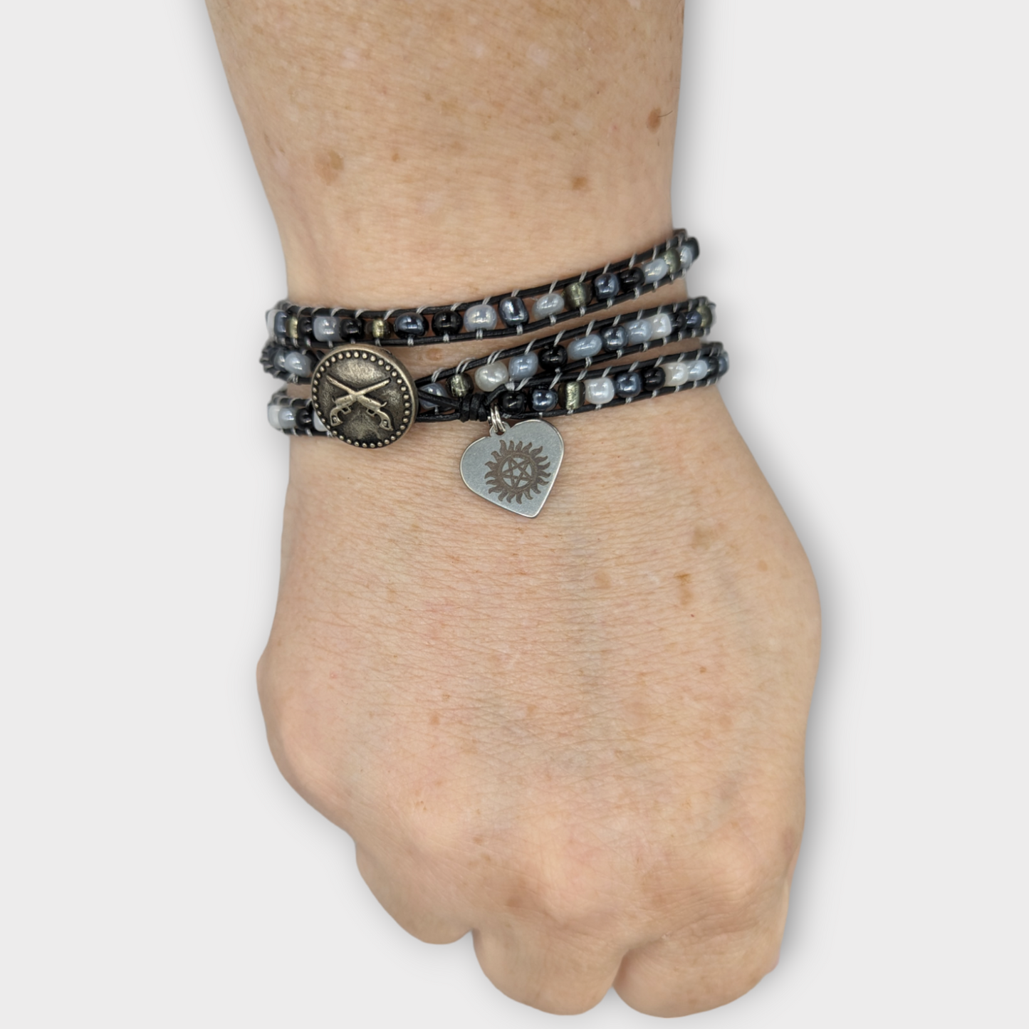 Beaded Wrap Bracelet with black, grey and white glass beads. Black leather cording, that is used for the crossed colts button and the Antipossession protection charm.