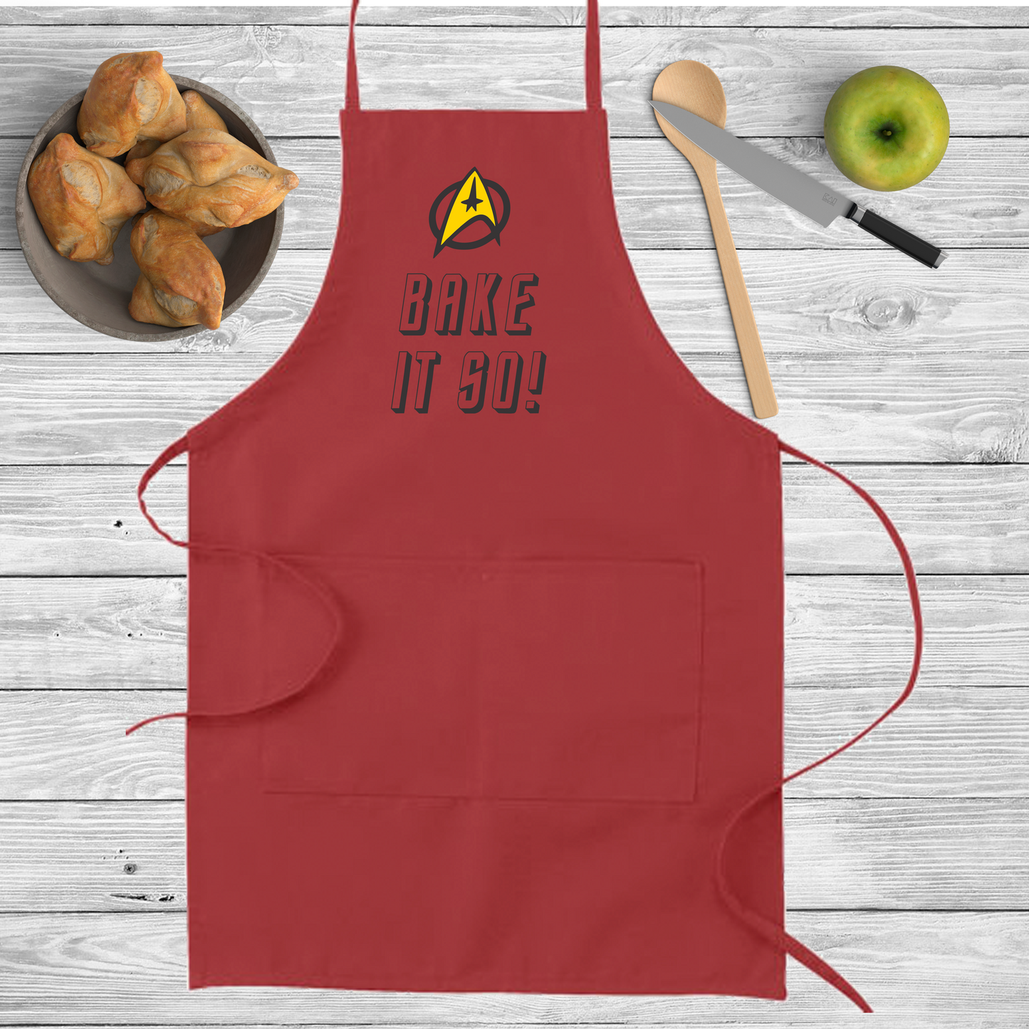 Red Apron with the Federation Logo and the words Bake it so! Written on it.